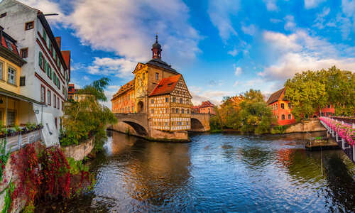 Amazing panoramic view of historic city center of Bamberg, Germany. Half-timbered Town Hall in the middle of rapid river, old buildings and bridge decorated by flowers. UNESCO World Heritage Site