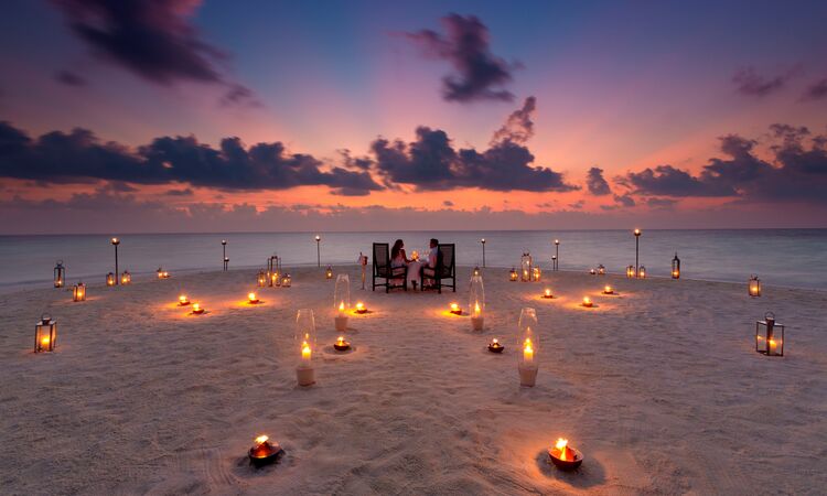 A couple enjoying a candlelit private sunset dining experience on the beach at Baros Maldives