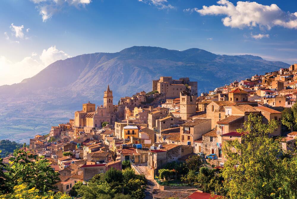 Caccamo, Sicily The beautiful hillside town of Caccamo in Sicily, shot a sunset with mountains in the background and a blue sky.
