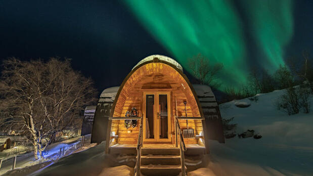 Northern Lights over wooden cabin at Snowhotel Kirkenes, Norway