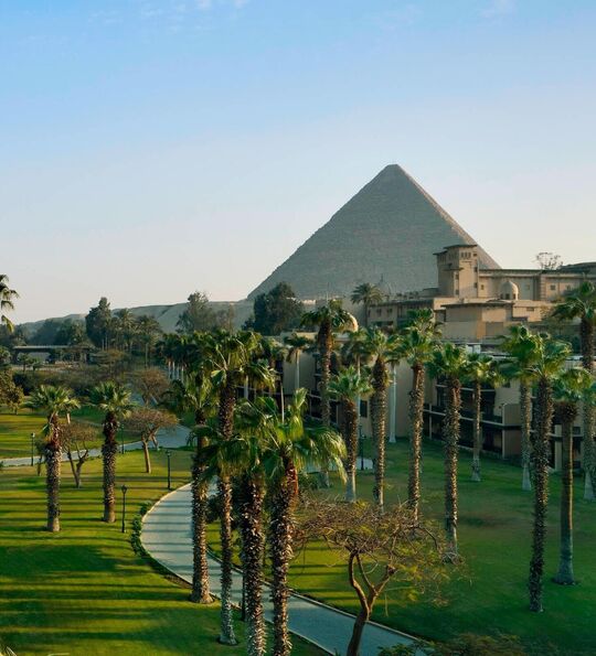 Grounds of the Marriott Mena House, Cairo, with palm trees and gardens in the foreground and the Pyramids of Giza beyond