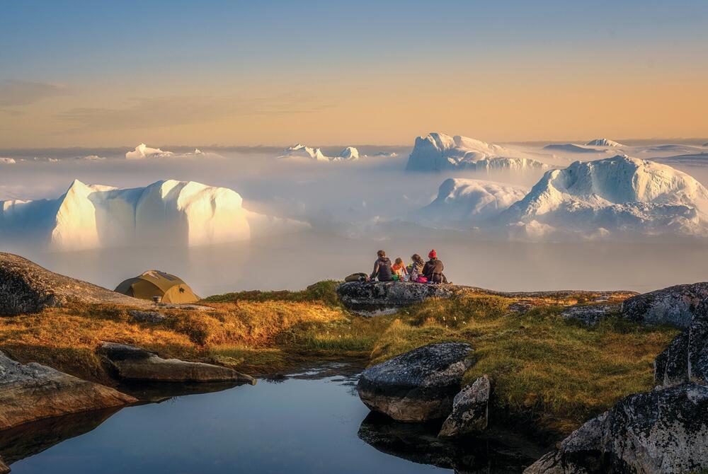 Ilulissat, Greenland A group of tourists looking out across icebergs rising from a misty sea near Ilulissat, Greenland