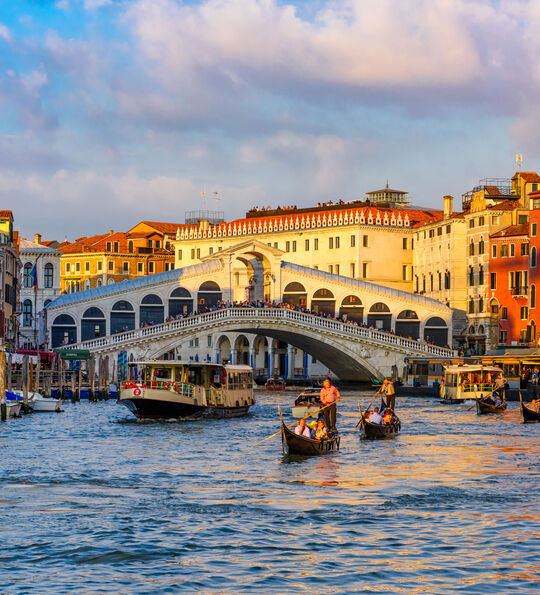A view of a sunlit Rialto Bridge on the Grand Canal in Venice