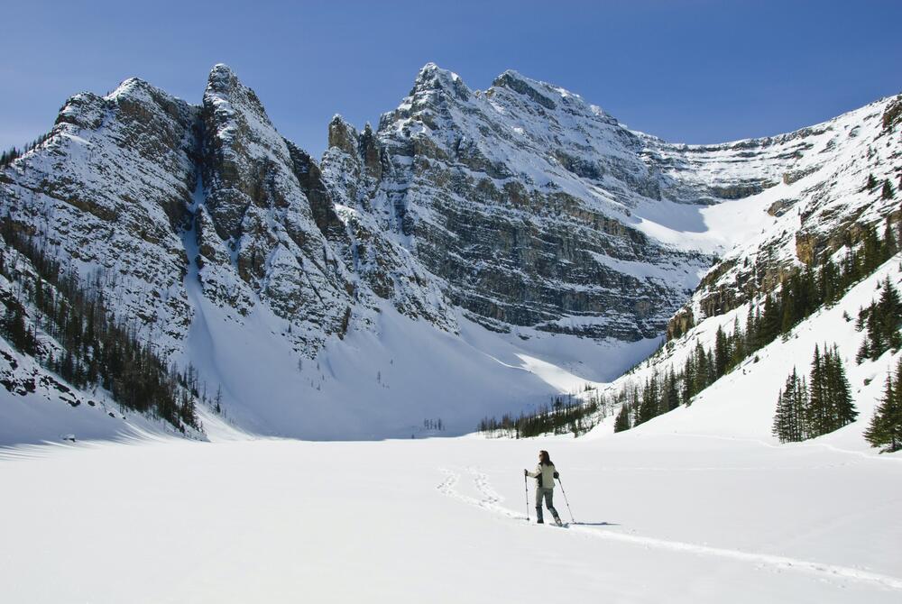A lady snowshoeing on a frozen lake in Banff National Park with snowy mountains behind.