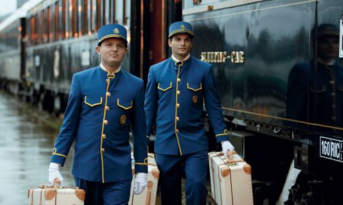 Cabin stewards, carrying luggage on the platform next to the Venice Simplon-Orient-Express, preparing for departure.