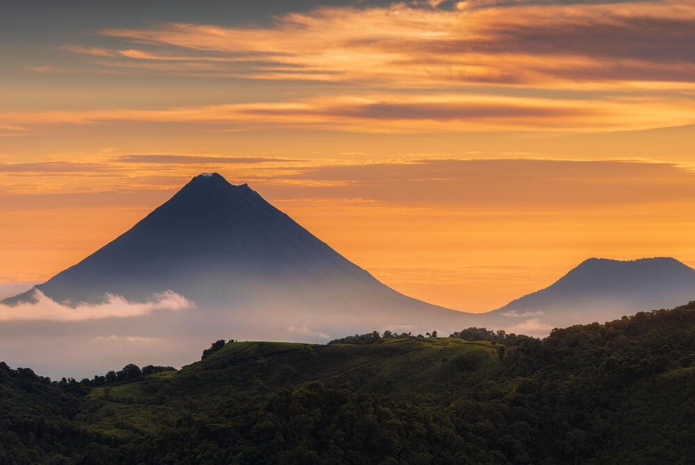 Sunset at Arenal Volcano, silhouetted against an orange sky